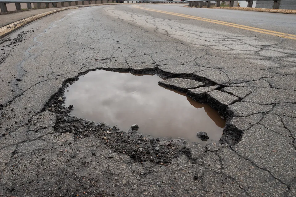 CLose-up of pothole in asphalt road filled with water reflecting grey cloudy sky.